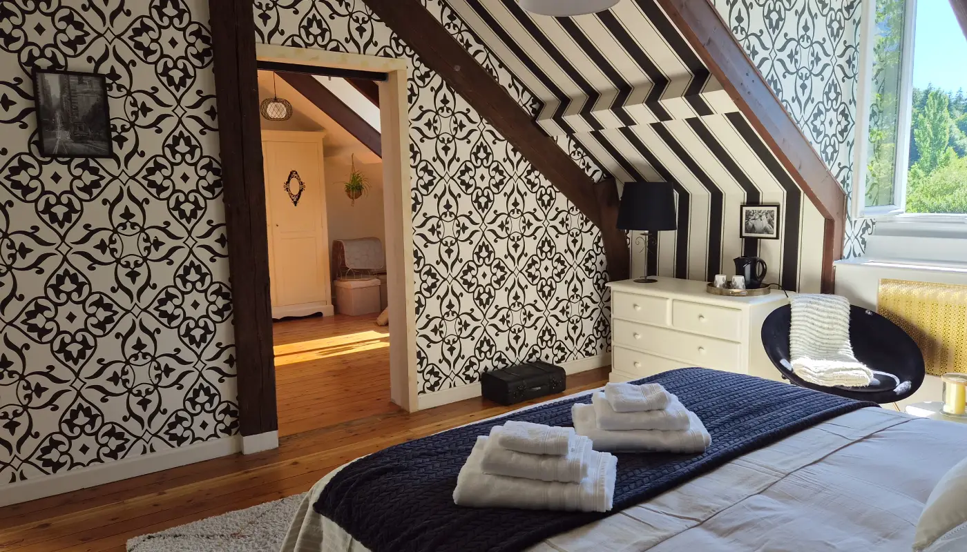 Vue d'ensemble de la chambre Papillon sous les combles, poutres apparentes et fenêtre donnant sur le jardin